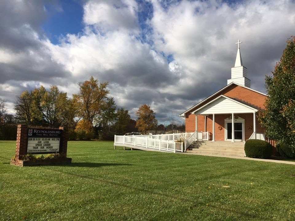 Reynoldsburg Free Will Baptist Church, with its brick exterior, white steeple, and flowering tree